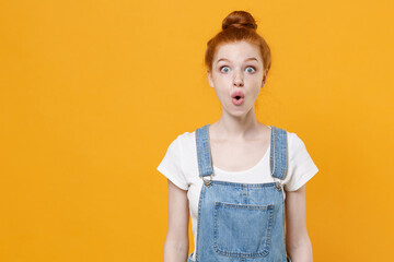 Shocked young readhead girl in casual denim clothes white t-shirt isolated on yellow wall background studio portrait. People sincere emotions lifestyle concept. Mock up copy space. Keeping mouth open.