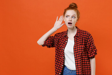 Shocked young readhead girl in casual red checkered shirt posing isolated on orange wall background...
