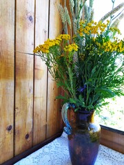 Wild field flowers yellow tansy and wheat ears on the background in the wooden wall by the window