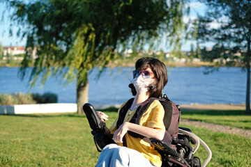 Disabled woman with muscular dystrophy in an electric wheelchair wearing a white face mask for...