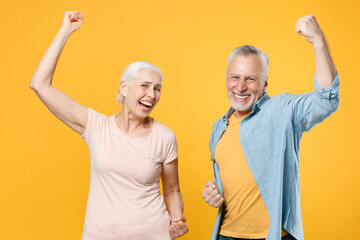 Joyful elderly gray-haired couple woman man in casual clothes posing isolated on yellow background studio portrait. People emotions lifestyle concept. Mock up copy space. Clenching fists like winner.