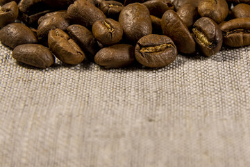 Roasted coffee beans lie on a linen texture fabric, selective focus, space for your text.
