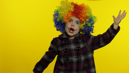 Little child girl clown in rainbow wig making silly faces. Having fun, smiling, dancing. Halloween