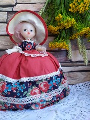 A bouquet of field yellow flowers tansy and wheat ears on a brick background and an old doll in a beautiful puffy dress