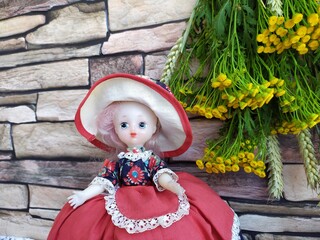 A bouquet of field yellow flowers tansy and wheat ears on a brick background and an old doll in a beautiful puffy dress