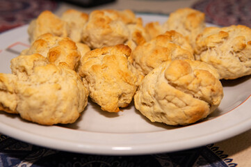 Un plato lleno de scones recien preparados. Puestos sobre una mesa y debajo de una luz calida