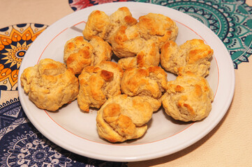 Un plato lleno de scones recien preparados. Puestos sobre una mesa y debajo de una luz calida