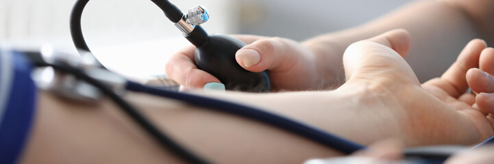 Close-up of persons hand on desk and doctor measuring blood pressure. Planned diagnostic. Modern equipment to examine circulation. Medicine and appointment concept