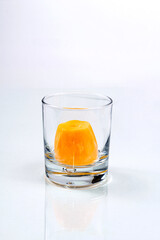 Glass with big piece of ice cube made of orange juice on the white background