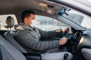 A young man sits behind the wheel wearing a mask for personal safety while driving during a pandemic and coronavirus. Epidemic