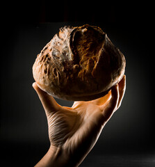 pan de masa madre sostenido en una mano sobre fondo obscuro