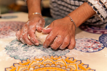 Joven mujer amasando una masa sobre una mesa enharinada, en el interior de una cocina.