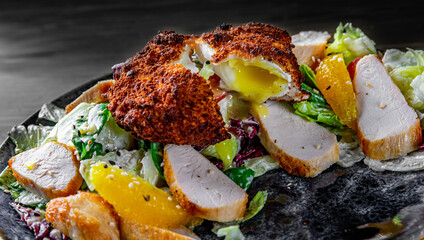 Salad with chicken, egg, tangerines and vegetables in plate on black wooden table background