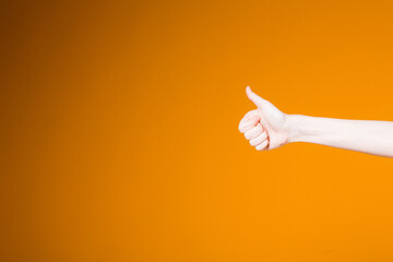 Female hand on an orange background shows a thumbs up in agreement and approval. Hand to use for banners and sites.