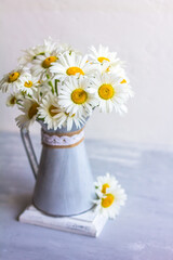 A bouquet of white daisies in a metal jug stands on a gray concrete table. Copy space for text