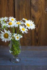 A bouquet of daisies in a glass vase stands on a wooden table.  Copy space for text