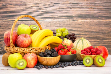 Group Healthy fresh fruit in a wooden basket, With vitamins c from bananas, kiwi, grapes, raspberries, blueberries, and blackberries, good for the body and diet food on the table in nature background.