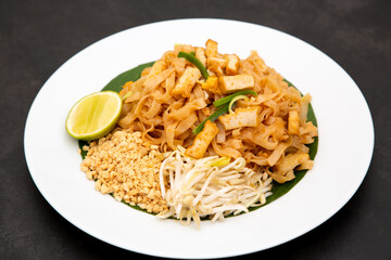Pad Thai is Thai food Noodle and tofu mixed with tamarind sauce and bean sprouts and spring onion in white dish put on the banana leaf in black background