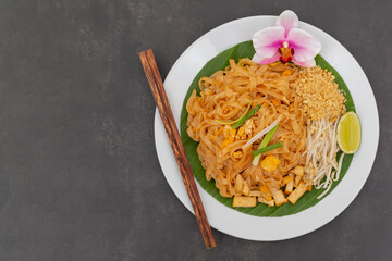 Pad Thai is Thai food Noodle and tofu mixed with tamarind sauce and bean sprouts and spring onion in white dish put on the banana leaf in black background