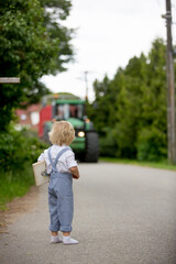 Blond toddler boy in vingate clothes holding book, standing on the street waiting for a bus