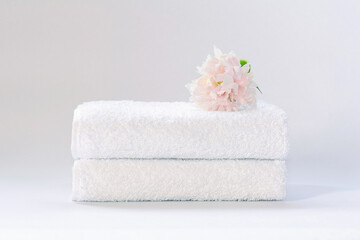 Obraz na płótnie Canvas Two white neatly folded terry towels with a delicately pink peony flower on a light background.