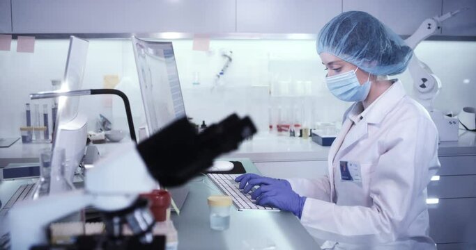Female scientist working in modern laboratory. Studying genetic material with microscope. Using computer