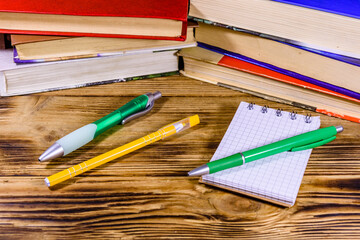 Fototapeta premium Opened small notepad and ball pens on a wooden table in front of stack of the books