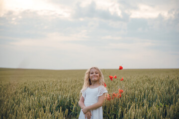 Fototapeta na wymiar beautiful little girl with blond hair in a white dress in the background of a beautiful field. Girl with a bouquet of red poppies