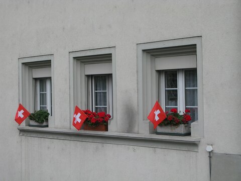 Beautiful Shot Of A Grey Building Facade With Switzerland Flags Near Three Windows