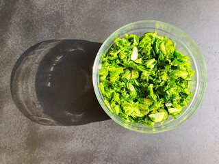 green lettuce and greens, cucumbers and lettuce, in a glass bowl, on a black wooden surface in sunlight, shadow