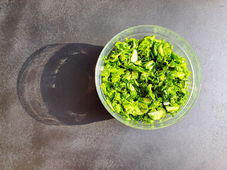 green lettuce and greens, cucumbers and lettuce, in a glass bowl, on a black wooden surface in sunlight, shadow