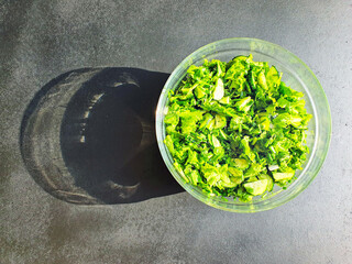 green lettuce and greens, cucumbers and lettuce, in a glass bowl, on a black wooden surface in sunlight, shadow