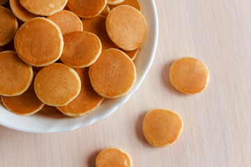 Trendy food - pancake cereal. Heap of mini cereal pancakes in bowl on bright background. Copy space for text or design.