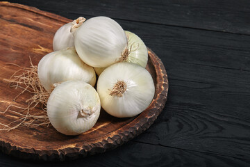 white onions on a wooden board on black background