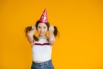 Young woman in a celebratory cap fooling around at a party on the yellow background