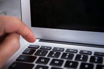 Pushing the esc switch on a keyboard of a grey notebook with a finger by male hand