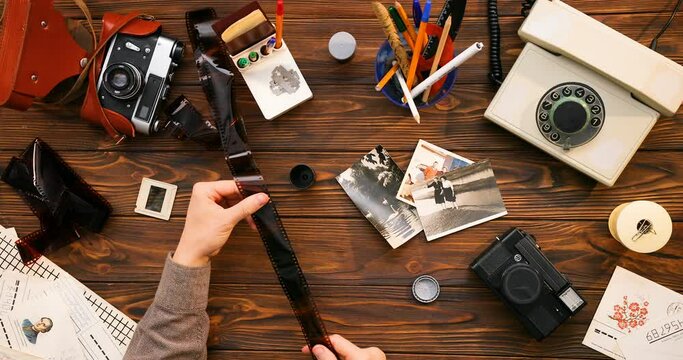 View from above on Caucasian male hands holding and looking through old films on wooden desk with photocameras and vintage stuff. Top view on desktop of photographer. Flat lay.