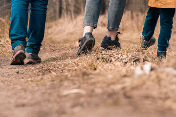 Family walks with children in forest path. Rear view on legs and shoes hikers. Walking boots and sneakers on ground and dry grass