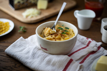 Homemade baked macaroni and cheese on wooden table surrounded by cheese, butter, milk, salt, pepper with shiny spoon scooping some of the dish.