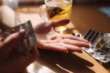 Close up of woman's hands hold pills. Hand with pills and black tea with lemon. Immunity. Vitamines
