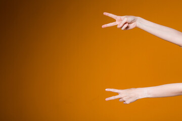 Female hands on the orange background show sign world index and middle fingers. Studio shot of slender gestures of hands