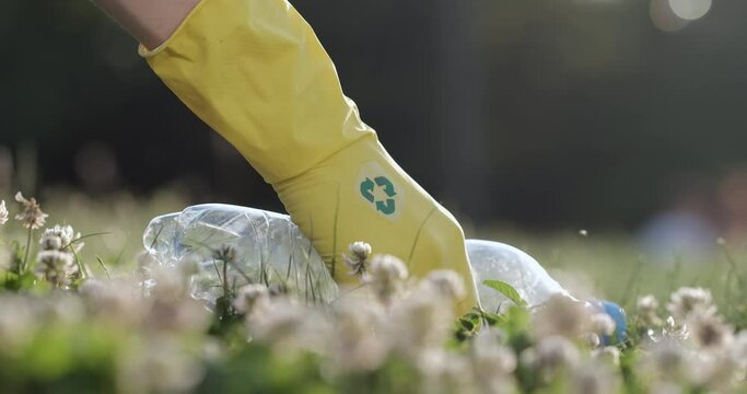 Close up of a plastic bottle, a man raises a plastic bottle with his hand in a yellow glove with a recycle sign.