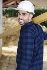 happy male carpenter with wooden plank at construction site