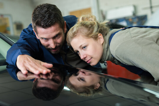 female and male car mechanic checking paint of a car