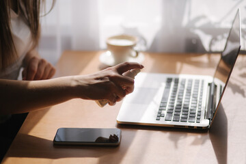 Close up woman hands using sanitizer gel dispenser at home. Home isolation, quarantine. Coronavirus concept. Female clean laptop using sanitizer