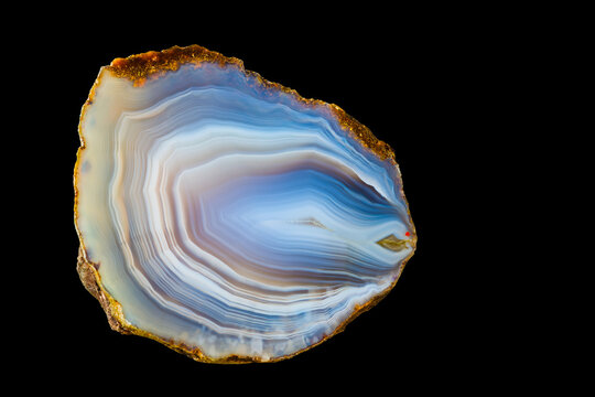 Close-up of polished agate gem with smooth icy surface texture isolated on black background. White-blue cut precious stone from north-east Czechia. Wavy pattern of concentric curves in cross section.