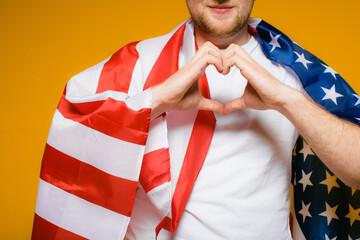 Celebrating an Independence day. Stars and Stripes. Young man with the flag of the United States of America isolated on yellow studio background. Looks happy and proud as a patriot of his country