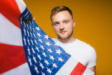Portrait of a happy young man with a beard , in casual clothes holding the us flag on a yellow background