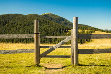highland rural scenic view wooden gate palisade paddock fence area with background mountain landscape in summer August day