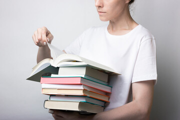 Girl in a white shirt holds a lot of books in the hands of a neutral background. Reading, page turning